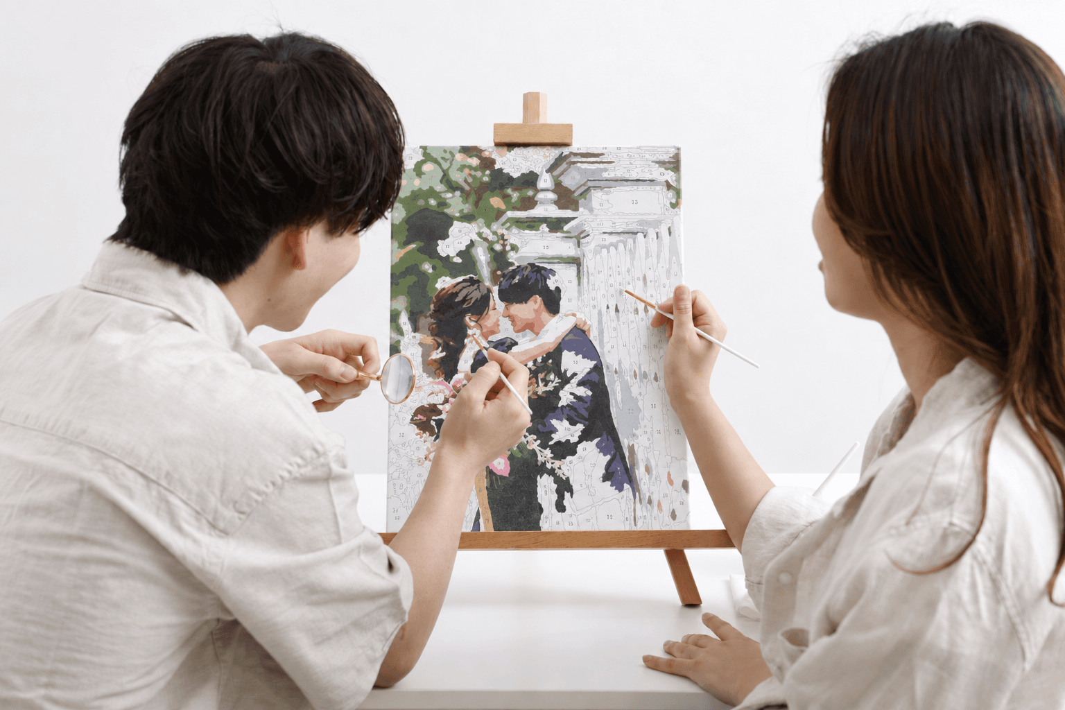 二人で人物のキャンバスに筆を入れ、少しずつ色を塗る制作風景